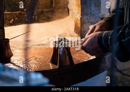 Mann Vorbereitung türkischen Kaffee in traditionellen Messing Töpfen, auf heißem Sand in einem Ofen zubereitet Stockfoto