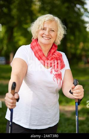 Ältere lächelnde Frau tut, Nordic Walking in der Natur im Sommer Stockfoto