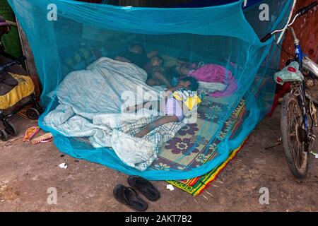 Eine arme Obdachlose scavenger Frau schläft unter einem Moskitonetz mit ihrer mittellosen jungen Kinder auf eine Stadt Bürgersteig in Kampong Cham, Kambodscha. Stockfoto