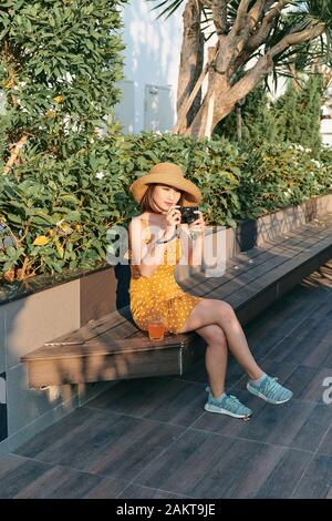 Modisch gekleidete Frau im Park sitzen und Kamera verwenden Stockfoto