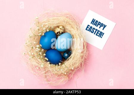 Ostereier in blauen Farben in einem Gelege auf dem rosafarbenen Hintergrund. Grußkarte. Stilvolles Design für Ostern, Null-Abfall-Konzept. Flaches Lay. Stockfoto