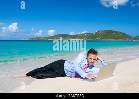 Entspannt Geschäftsmanns, der auf seinem Laptop liegen im Freien am Ufer eines hellen tropischen Strand Stockfoto