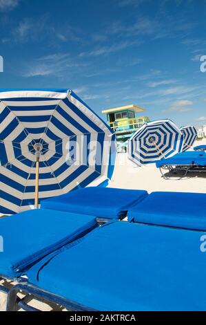 Blau-weiß gestreifte Sonnenschirme, die neben Sonnenliegen am Miami Beach ruhen Stockfoto