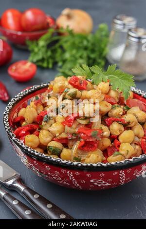 Garnitur von Kichererbsen mit Paprika und Tomaten, ein vegetarisches Gericht reich an Protein, bei einer Platte gegen einen dunklen Hintergrund entfernt, vertikale Ausrichtung Stockfoto