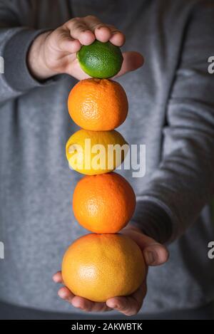 Frische Zitrusfrüchte stapeln sich in den Händen des Mannes. Köstliche saftige Fruchtsäule. Grapefruit, Orange, Zitronen und Kalkhaufen. Gesunde Ernährung. Veganismus Konzept Stockfoto