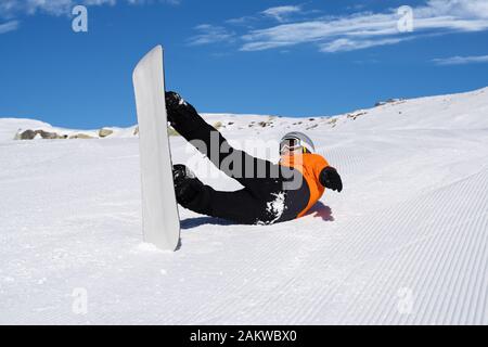 Ein Mann in Orange Jacke Fallen beim Reiten Snow Board auf Schnee, Anschluss Stockfoto