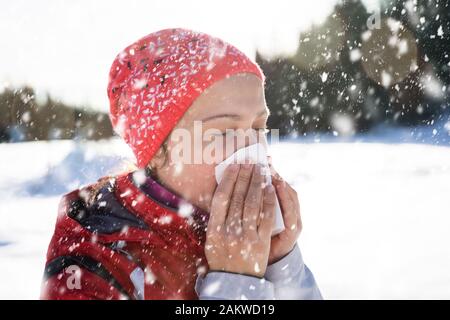 Hübsche junge Frau bläst Ihre Nase mit einem Taschentuch Outdoor im Winter Stockfoto