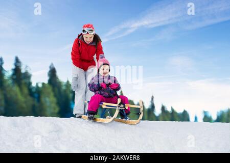 Junge Mutter schob ihren niedlichen Tochter auf Schlitten über verschneite Landschaft Stockfoto