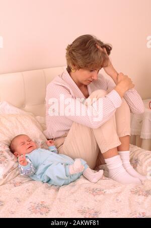 Junge Mutter mit einem Baby, das an einer postnatalen Depression leidet, traurig aussieht und auf einem Bett sitzt Stockfoto