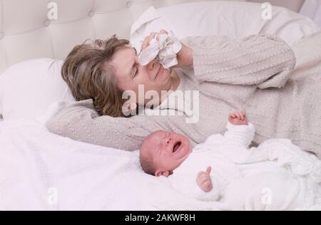 Junge Mutter mit einem Baby, das an einer postnatalen Depression leidet, weinend, auf einem Bett liegend Stockfoto