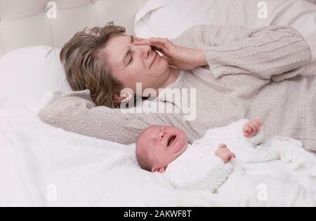 Junge Mutter mit einem Baby, das an einer postnatalen Depression leidet, weinend, auf einem Bett liegend Stockfoto