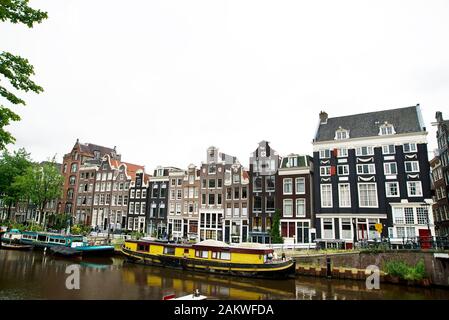Die Seite des Amsterdamer Kanals zeigt traditionelle Seitenhäuser mit gelber Kahn, die auf dem Kanal vergraben sind Stockfoto