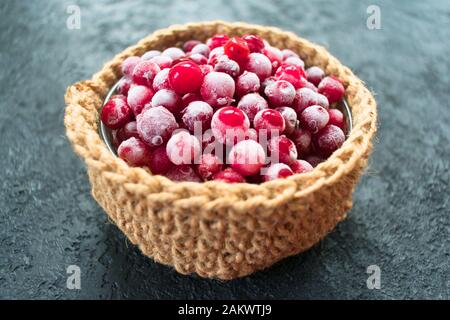 Gefrorene Preiselbeeren in einem kleinen Korb auf schwarzem Grund. Stockfoto