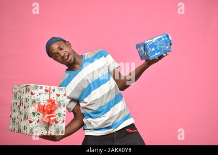 Aufgeregter junger schwarzer Mann mit zwei Geschenkschachteln, einem großen und schweren, einem kleinen und leichteren Stockfoto