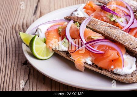 Gehärteter Lachs ganze Weizenbaguette Sandwiches, Brot mit Quark, geräucherter Fisch, rote Zwiebel, Avocado auf rustikalem Tisch in der Nähe Stockfoto