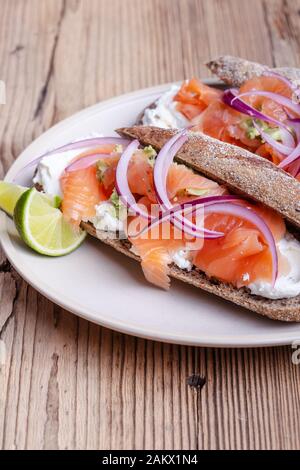 Gehärteter Lachs ganze Weizenbaguette Sandwiches, Brot mit Quark, geräucherter Fisch, rote Zwiebel, Avocado auf rustikalem Tisch in der Nähe Stockfoto