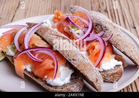 Gehärteter Lachs ganze Weizenbaguette Sandwiches, Brot mit Quark, geräucherter Fisch, rote Zwiebel, Avocado auf rustikalem Tisch in der Nähe Stockfoto