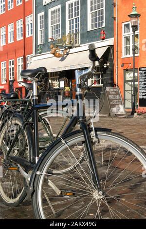 Schwarze Fahrräder parkten aufrecht auf der Seite des Nyhavn Hafen in Kopenhagen vor einem am Meer gelegenen Restaurant Havfruen im Winter. Stockfoto