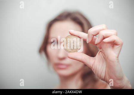 Frau zeigt, dass sie eine Bitcoin in der Hand auf einem Gesichtshintergrund hält. Stockfoto