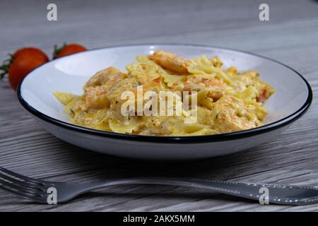 Italienische Pasta in cremiger Soße mit Garnelen auf dem Teller, Draufsicht. Pasta in Form von Bögen auf Holzgrund Stockfoto