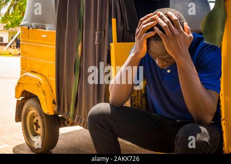 Junger afrikanischer Mann, der in einer Rikscha sitzt und seinen Kopf hält Stockfoto