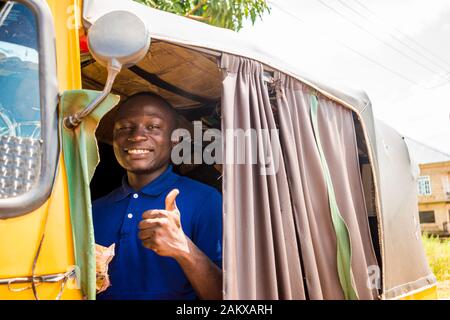 Junger afrikanischer Mann, der ein Rikscha-Taxi fährt und dabei sein Geld mit einem Lächeln auszählt, der einen Daumen nach oben gibt Stockfoto