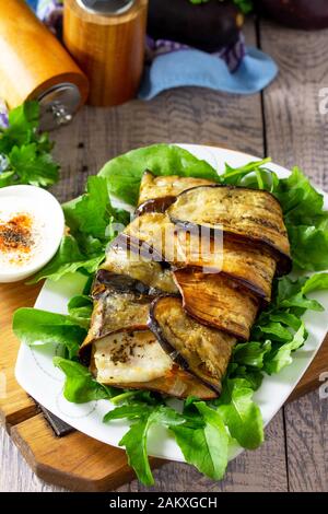 Leckerer Fisch, der mit Gemüse in Auberginen gebacken wird und mit Paprika-Joghurt-Sauce auf einem Holztisch serviert wird. Stockfoto