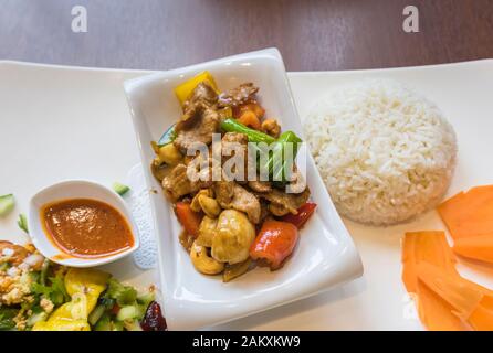 Traditionelle thailändische Mahlzeit, eine Cashew Pfannengerichte Rindfleisch Teller serviert in einem whit Schüssel auf eine China Platte mit gedämpftem Reis und Möhren und Gemüsegarnitur Stockfoto