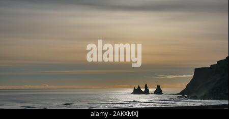 Vik Strand bei Sonnenuntergang, Island, mit Meer-Stacks und Cliff auf niedrigen Horizont und Moody gelb Abend Winter sky Stockfoto