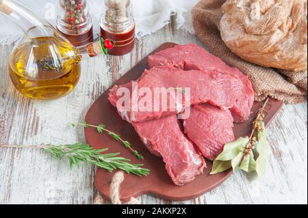 Fleischstücke sind bereit für Marinade liegen auf einer Tontafel mit Gewürzbachtblatt, Pfeffer, provenzalischen Kräutern. Stockfoto