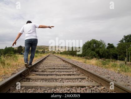 Unkenntlich junger Mann balanciert auf den Bahngleisen in einer ländlichen Szene an einem bewölkten Tag. Tandil, Buenos Aires, Argentinien. Stockfoto