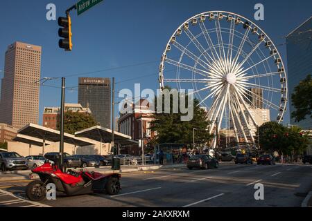 Horizontaler Schuss eines roten Autos mit drei Rädern im Centennial Olympic Park Dr mit dem Skyview Atlanta Ferris Rad hinten, Atlanta, Georgia, USA Stockfoto