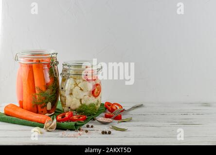 Zwei Glasgefäße aus fermentiertem Blumenkohl, Karotten, Gemüse auf hellem Hintergrund. Mit Textilhellgrau. Fermentation ist eine Quelle für Probiotika. Stockfoto