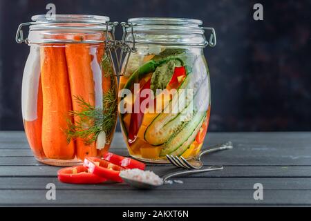 Zwei Glasgefäße aus fermentierten Gurken, Karotten, Pfeffer, Salz, Gemüse auf dunklem Hintergrund.Fermentation ist eine Quelle von Probiotika. Beliebte Vegetari Stockfoto