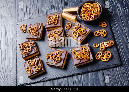 No-Bake Chocolate Peanut Butterbars mit Brezel-Crackern auf einem Schiefertablett auf einem Holztisch, Ansicht von oben Stockfoto