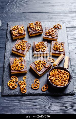 No-Bake Chocolate Peanut Butterbars mit Brezel-Crackern auf einem Schiefertablett auf einem Holztisch, vertikale Ansicht von oben Stockfoto