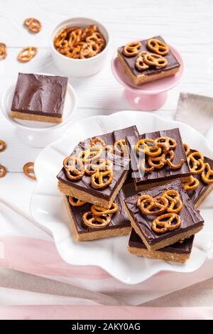 Nahaufnahme der No-Bake Chocolate Peanut Butterbars mit Brezelknackern auf einem Kuchenständer auf einem weißen Holztisch, Ansicht von oben Stockfoto