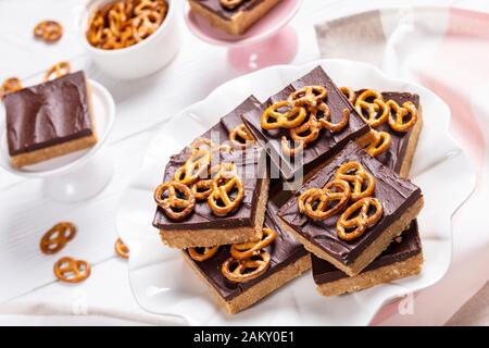 Nahaufnahme von Schokoladen-Peanut-Butterbars mit Brezel-Crackern auf einem Kuchenständer auf einem weißen Holztisch, Ansicht von oben Stockfoto