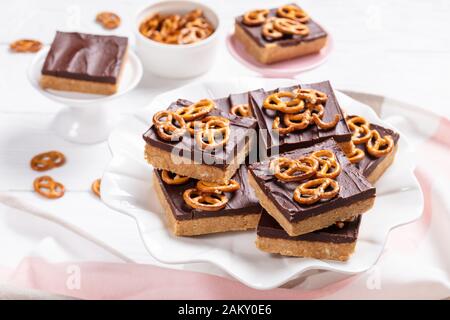 Nahaufnahme von Schokoladen-Peanut-Butterbars mit Brezel-Crackern auf einem Kuchenständer auf einem weißen Holztisch, Ansicht von oben Stockfoto