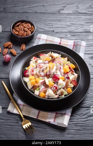 Frischer apfelsalat mit Trauben, Sellerie, Cheddar-Käse und Pekannüssen mit Mayonnaise-basiertem Dressing auf schwarzen Tellern auf einem Holztisch, vertikaler Ansicht Stockfoto