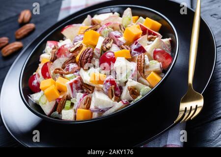 Nahaufnahme von frischem waldorfsalat aus Trauben, Sellerie, Cheddar-Käse und Pekannüssen mit Mayonnaise-Dressing in schwarzer Schüssel auf einem Holztisch Stockfoto