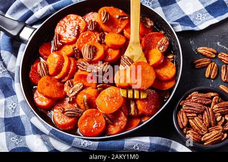 Kandierte Süßkartoffeln mit braunem Zucker, Ahorn-Sirup, Orangensaft und Pekannüssen in einem Skillet auf einem Betontisch mit Küchentuch, Blick aus Abo Stockfoto