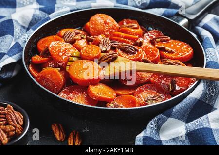 Nahaufnahme von Kandierten Süßkartoffeln mit braunem Zucker, Ahorn-Sirup, Orangensaft und Pekannüssen in einem Skillet mit Holzspachtel, Ansicht von oben Stockfoto