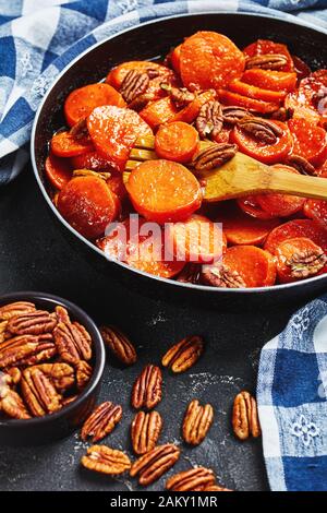 Nahaufnahme von Kandierten Süßkartoffeln mit braunem Zucker, Ahorn-Sirup, Orangensaft und Pekannüssen in einem Skillet mit Holzspachtel, vertikaler Ansicht von Abo Stockfoto