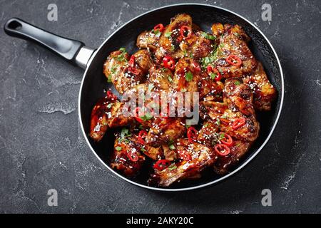 Teriyaki-Hühnerflügel bestreut mit Sesamsamen, Chili Pfefferstücken und Petersilie in einem Skillet auf einem Betontisch, horizontale Ansicht Stockfoto