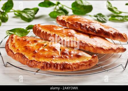 Nahaufnahme von frisch gebackenen Kalzonen, verschlossenen Pizzen mit Spinat und Käsefüllung auf einem Drahtgestell auf einem Holztisch, italienische Küche Stockfoto