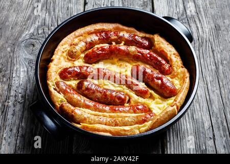 Nahaufnahme von "Toad in the Hole", "Wurst Toad", traditionelles englisches Gericht, bestehend aus Würstchen in Yorkshire Pudding-Teig in schwarzer keramischer Backform Stockfoto