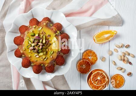 Köstlicher feuchter Kürbis-Karotten-Biskuit mit orangefarbener Glasur, mit Pistazien auf Keramikständer auf einem weißen Holztisch bestreut, flach Stockfoto