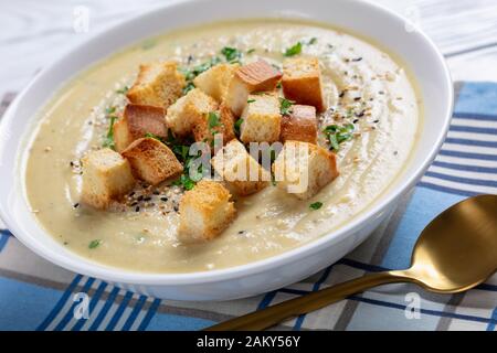 Nahaufnahme einer Portion Asiago Gerösteter Knoblauchkaulblumensuppe mit Croutons in einer weißen Schüssel auf einem Holztisch, horizontale Ansicht von oben Stockfoto