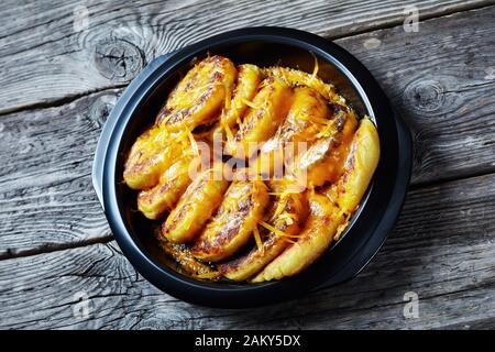 Nahaufnahme hausgemachter Kartoffelkuchen mit geriebenem Cheddar-Käse in einem schwarzen Gericht auf einem rustikalen Holztisch Stockfoto